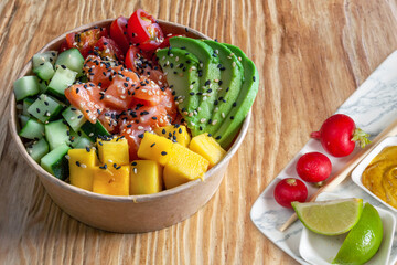 Takeaway poke bowl with fresh salmon, avocado, mango and vegetables in recycled kraft paper...