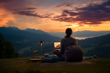 Serene Sunset Work Environment in Nature. Woman using laptop in a tranquil outdoor setting as the sun sets behind the mountains.