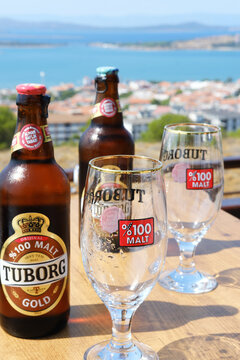 Beer Bottles and Empty Glasses with Ocean Backdrop. Vertical shot of Tuborg Gold beer bottles and empty glasses on a wooden surface, overlooking a vibrant ocean view. Cunda, Turkey - August 26, 2023