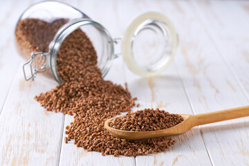 Raw buckwheat in wooden scoop and in glass storage jar on a white wooden table.