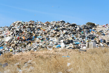 Large Heap of Garbage at City Dump with Clear Sky. Massive pile of mixed waste dominates the city dump under a bright clear sky, with dry vegetation around.