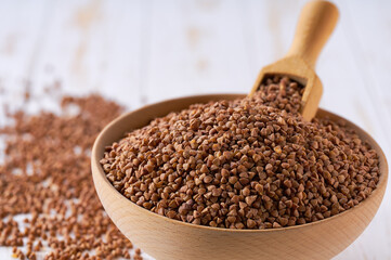 Raw buckwheat are scattered in a wooden bowl close up.