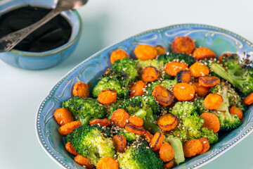 Asian-style stir-fried broccoli with carrot. The dark sauce in a small bowl with a spoon in the upper left corner.