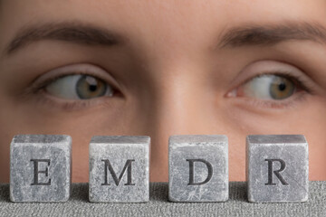 Letters EMDR written on grey stone cubes blocks. Close-up woman's face with eyes looking left.  Eye...