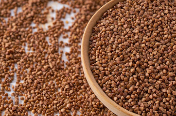 Organic buckwheat are scattered out of the wooden bowl on a light table, selective focus.