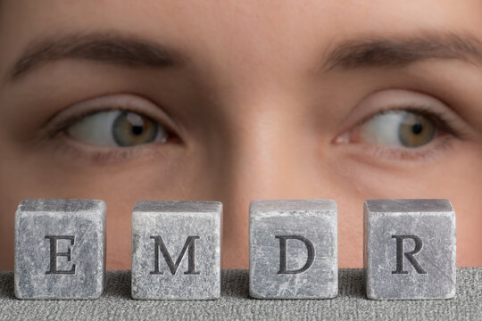 Letters EMDR written on grey stone cubes blocks. Close-up woman's face with eyes looking left.  Eye Movement Desensitization and Reprocessing psychotherapy treatment concept.