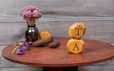 Letters TE written on wooden irregular blocks lying on a round table with dried flowers and other...