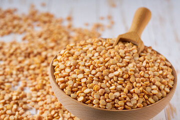 Organic raw dried peas are scattered in a wooden bowl close up.