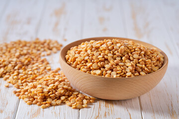 Dry yellow peas are scattered out of the wooden bowl on a light table, selective focus.