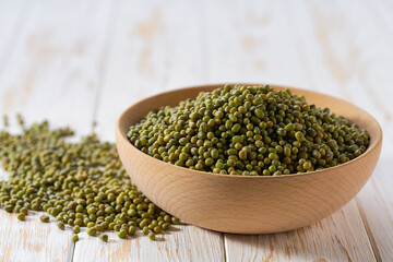 Green mung beans in a wooden bowl on a white wooden table.