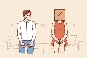 Indecisive man sits near woman with paper bag on head and is afraid of becoming acquainted. Indecisive guy sits on sofa with girlfriend, and is stressed due to timidity interfering with relationships