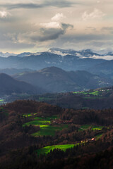 A scenic view over the valley and the mountains in the background. Green sun lit patches of grass in the valley beneath in the sunset.