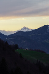 Obraz premium A three peaked mountain in the sunset with cloud cover over them and a small houde in front.