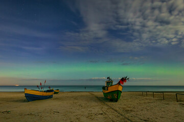 Northern lights over the Baltic Sea beach in Jantar with fishing boats, Poland. - 767375149