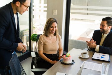 Beautiful woman making a wish and looking at her birthday cake she got at the office