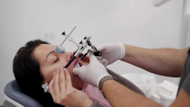 Orthodontist installing dental facebow on woman face in modern dental office. Dentist installs facebow on female patient to get information of the patient's dentition. Modern cosmetic dentistry.