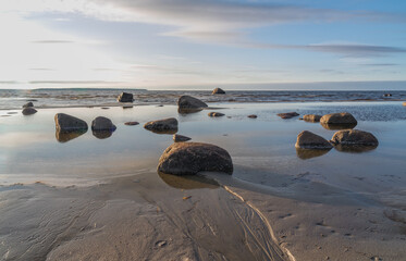 Andineeme Estonia - March 25 2024: Southern coast of the Finnish Gulf. Smooth transparent reflective water and granite rocks. Golden hour. Orange sunset markings under the low altitude clouds. 