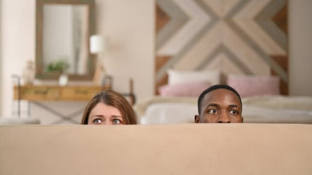 Young couple, woman and man comically hiding behind the sofa, close up