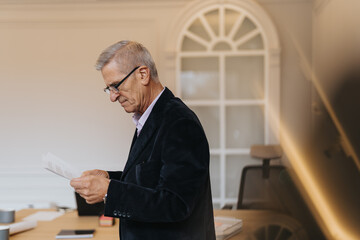 Fototapeta premium Mature businessman reading paperwork, analyzing reports, statistics or teamwork results at modern office setting.