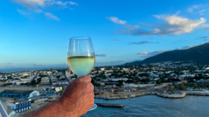 A man holding a glass of white wine with a blurred aerial view of Puerto Plata, Dominican Republic in the background.