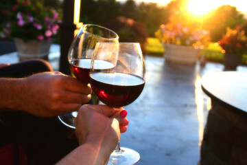 Two people couple enjoying red wine outdoors on a patio at sunset golden hour