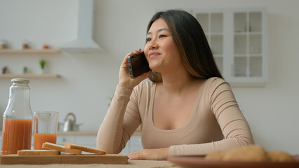 Asian woman talk mobile phone in home kitchen multiethnic chinese japanese girl chatting with friend smiling answer call talking discussing news speaking cellphone laughing make order food delivery