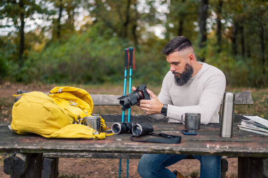 Photographer in his 30s reviewing his hiking adventure photos while sitting on a park bench in the woods.