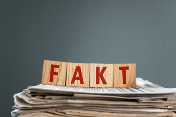 Newspapers on wooden cubes with "fact" written on them, on gray background, stock photo