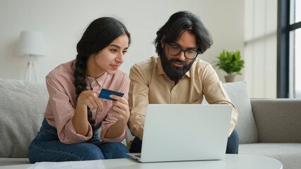 Arabian Indian muslim couple family sit on sofa in living room home office use credit bank card...