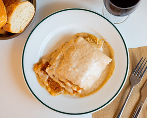 On set table there is plate with hearty and delicious dish - meat lasagna. Food is cooked in oven from puff pastry and layer of minced meat, grated cheese and sauce