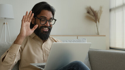 Smiling Arabian Indian muslim man talking virtual on laptop greet colleagues talk webcam video call...