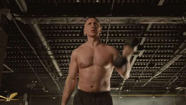 A barechested athlete lifts dumbbells to build muscle in the gym
