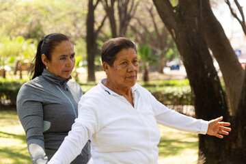 Two Women Standing Together performing fitness movements in a green and bright park 