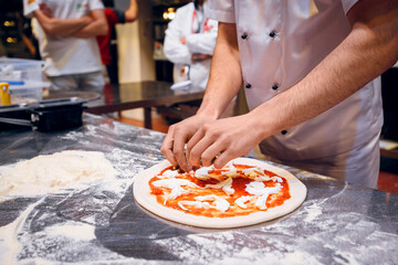 Pizzaiolo prepares pizza Margarita. knead the dough with your hands, add tomato sauce and mozzarella cheese. traditional italian food
