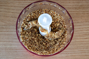 ground peanuts in a plastic blender with a gray metal knife on a wooden table background.