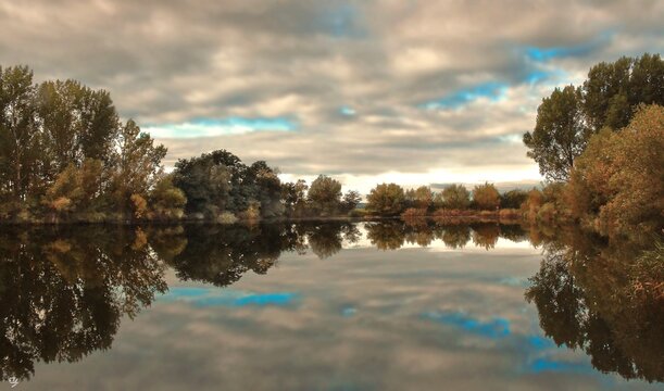 Nature in autumn with trees in autumn colors located next to the lake and a beautiful reflection of the scene in the lake with cloudy sky