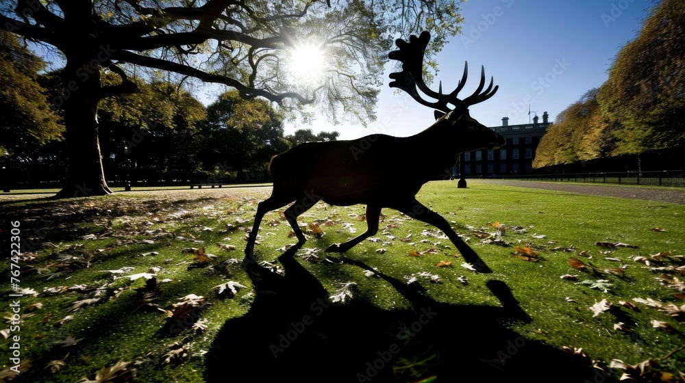 Canvas Prints a statue of a deer in the middle of a grassy area with leaves on the ground and a building in the ba