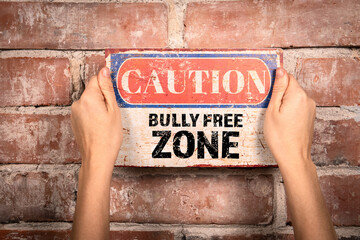 Bully Free Zone. Caution sign in a woman's hand on a brick background
