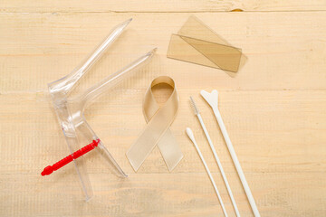 Beige ribbon with gynecological tools on light wooden background. Uterine cancer awareness concept
