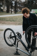 A young male entrepreneur is engaged in fixing his bicycle in a tranquil park setting, showcasing a blend of business and leisure.