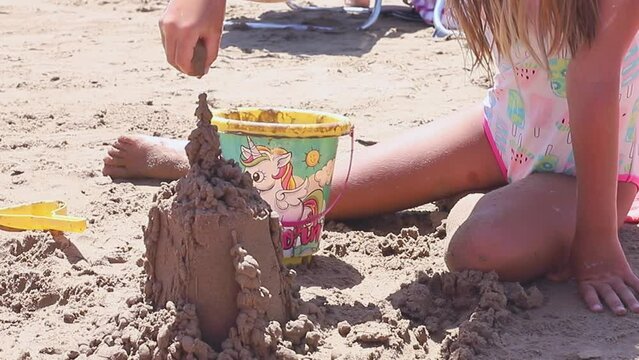 Close up of kids hands building sandcastle on the beach during sunny summer day.