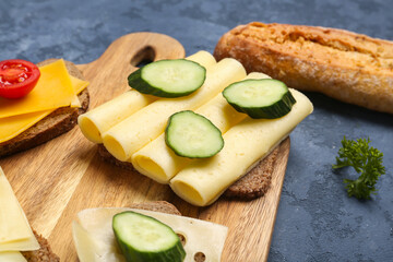 Tasty sandwich with cheese and cucumber in board on blue background, closeup