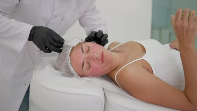 Performing thread face lifting in medical center. Cosmetologist performs thread lifting procedure to rejuvenate face. Concept Rejuvenation, cosmetology, innovation. Concept Rejuvenation, cosmetology
