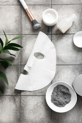Obraz premium Facial sheet mask with different cosmetic products and leaves on grey tile background