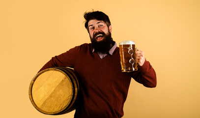 Beer time. Happy brewer with wooden barrel and mug of beer. Bearded man tasting brewed beer in pub...