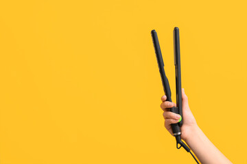 Female hand with straightening iron on yellow background.