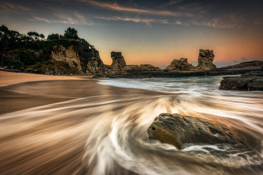 Beautiful sunrise beach showing water flow path foreground around the rocks with golden hours sky