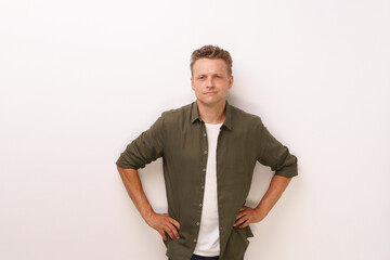 A man in a green shirt and white shirt stands with his arms crossed. He looks serious and is staring at the camera