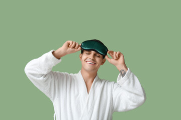 Portrait of handsome young man in bathrobe and sleeping mask on green background