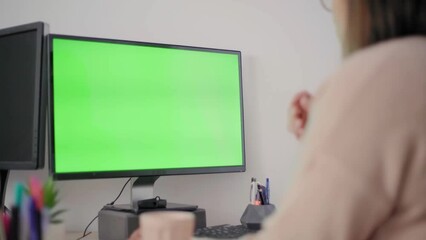 A woman sitting by a computer and using a smartphone application to work on personal finance at home